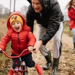 Father helping son ride a bicycle on a fall day while mother and daughter watch.