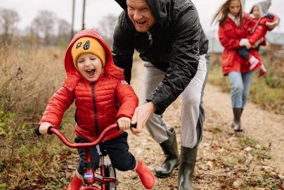 Father helping son ride a bicycle on a fall day while mother and daughter watch.